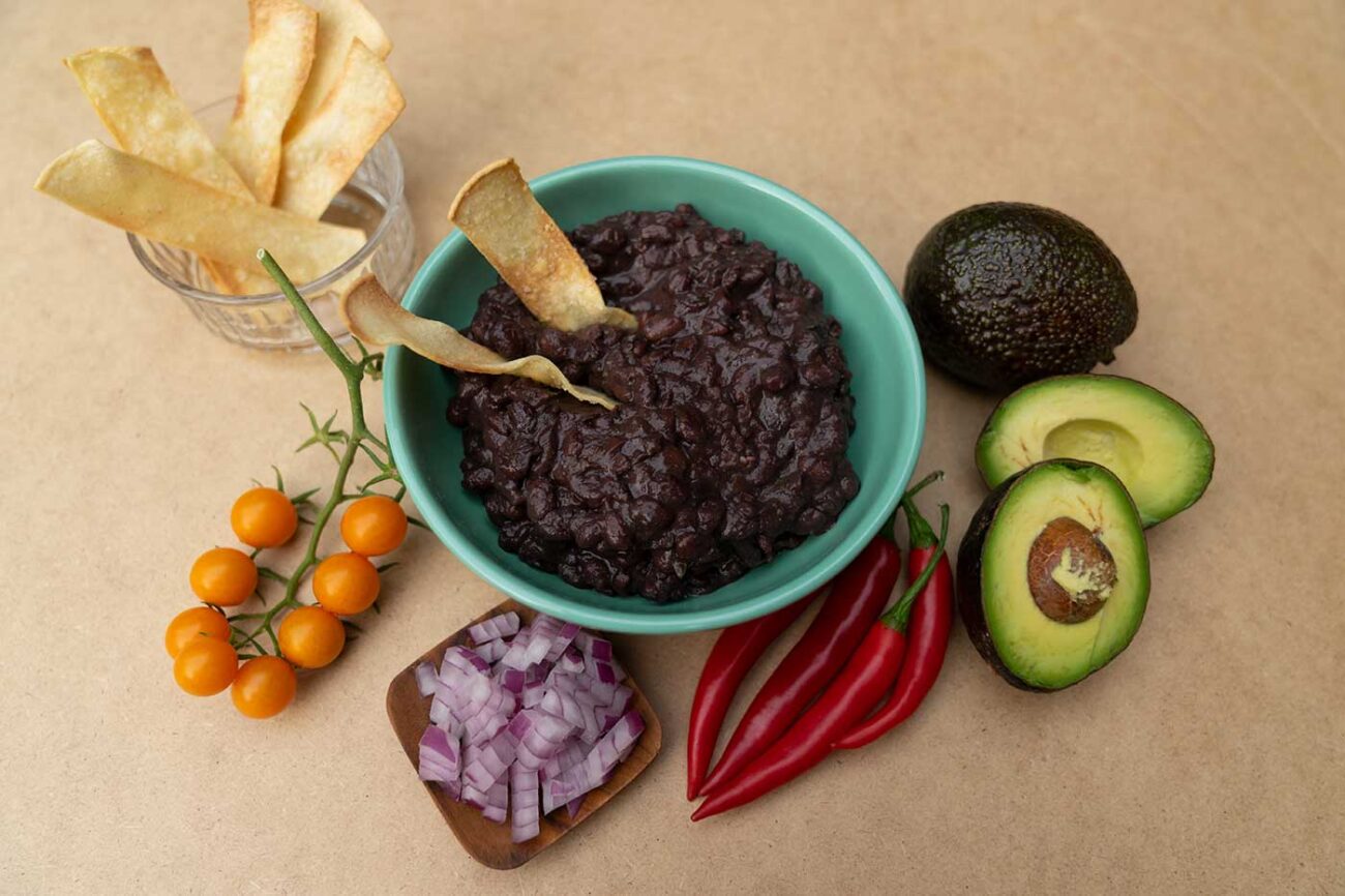 black bean recipe cooked up in a bowl with tomatoes red peppers avocado and red onion on the side for garnish