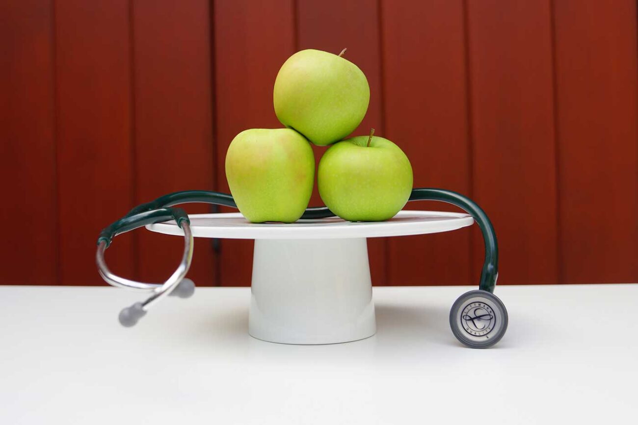 vegan health benefits three green apples on a pedestal with a stethoscope