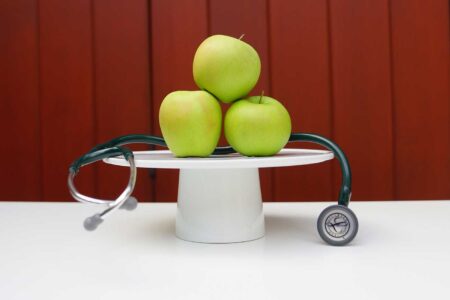 vegan health benefits three green apples on a pedestal with a stethoscope