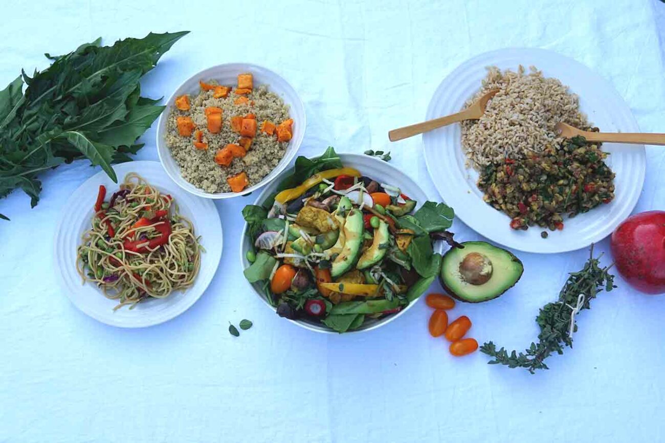 Table of healthy vegan food including a salad with seasoned tofu whole wheat pasta quinoa legumes and brown rice