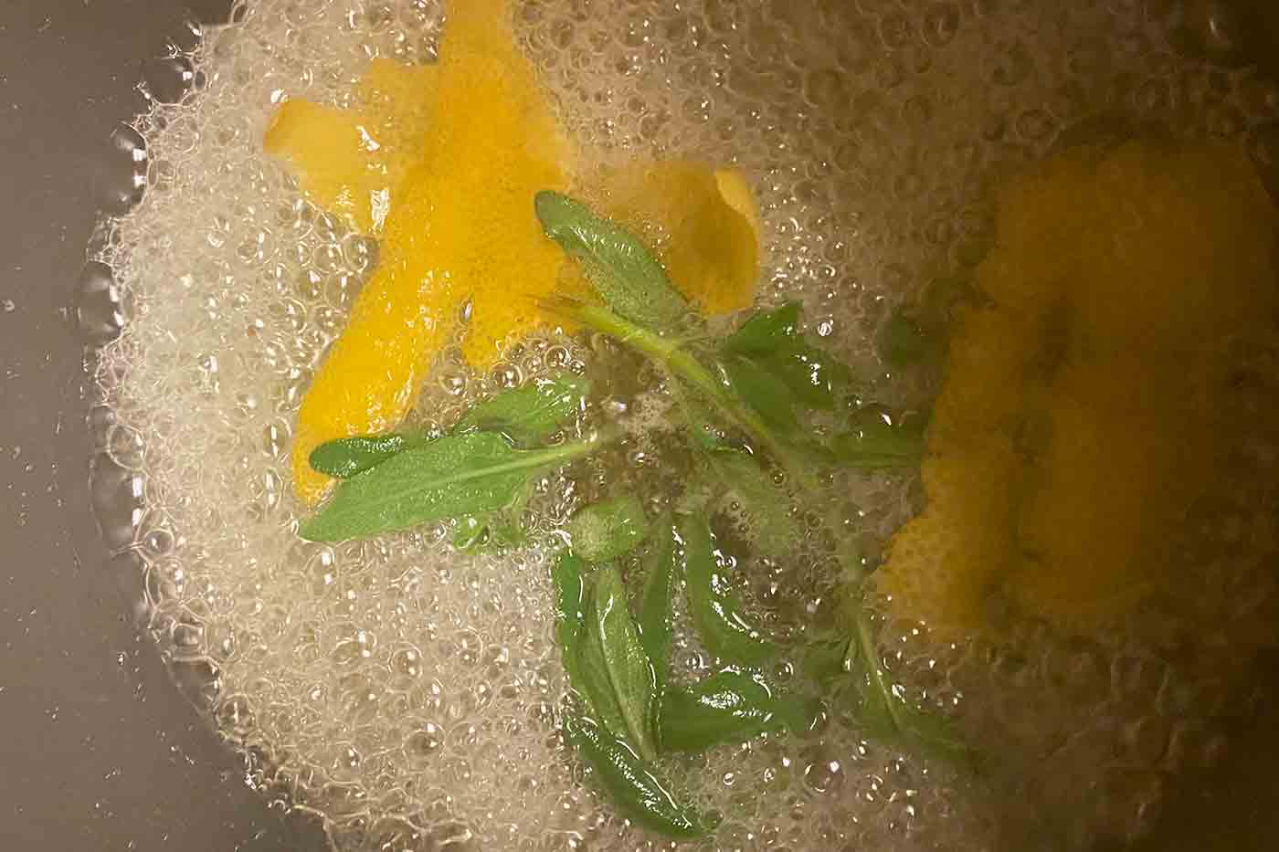 bubbling home made simple syrup in a pan on the stove with lemon and sage