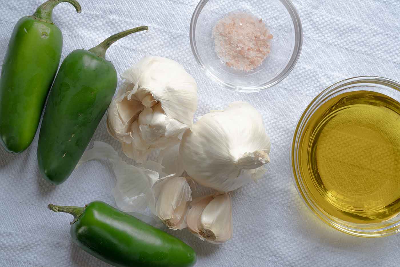 jalapeno peppers and garlic next to a bowl of pink salt and a bowl of oil