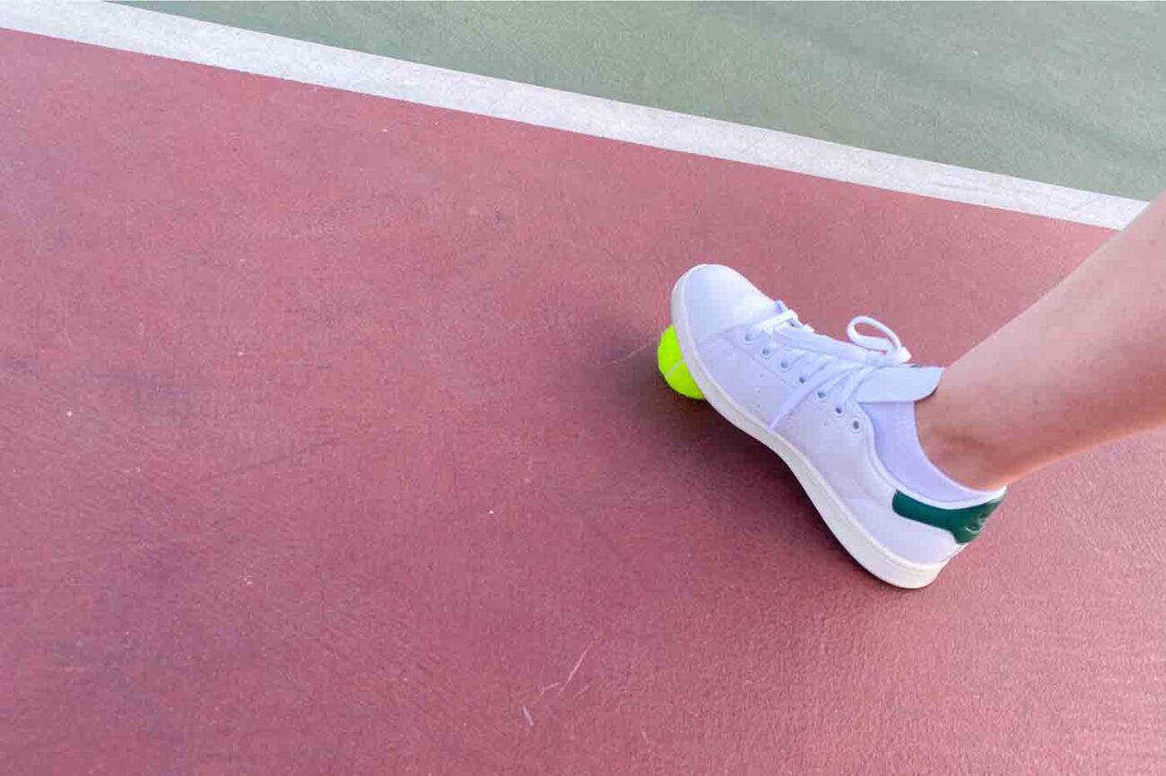 vegan Stan Smith tennis shoes from Adidas modeled on a tennis court with a tennis ball