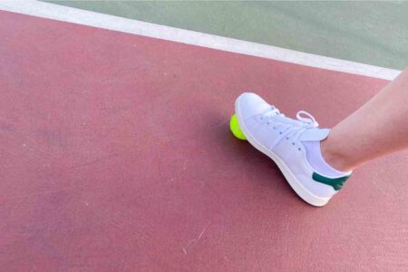 vegan Stan Smith tennis shoes from Adidas modeled on a tennis court with a tennis ball