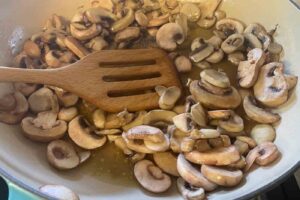 sliced mushrooms cooking in oil in a Le Creuset pan for Christmas lima bean salad recipe